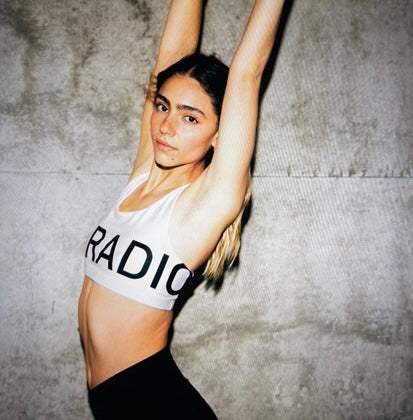 Woman wearing Authentic AF Sports Bra with logo front and back against concrete wall