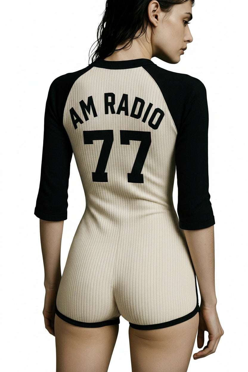 Back view of a model wearing The 77 Onesie in black and cream stretch rib fabric with "AM RADIO 77" printed on the back.