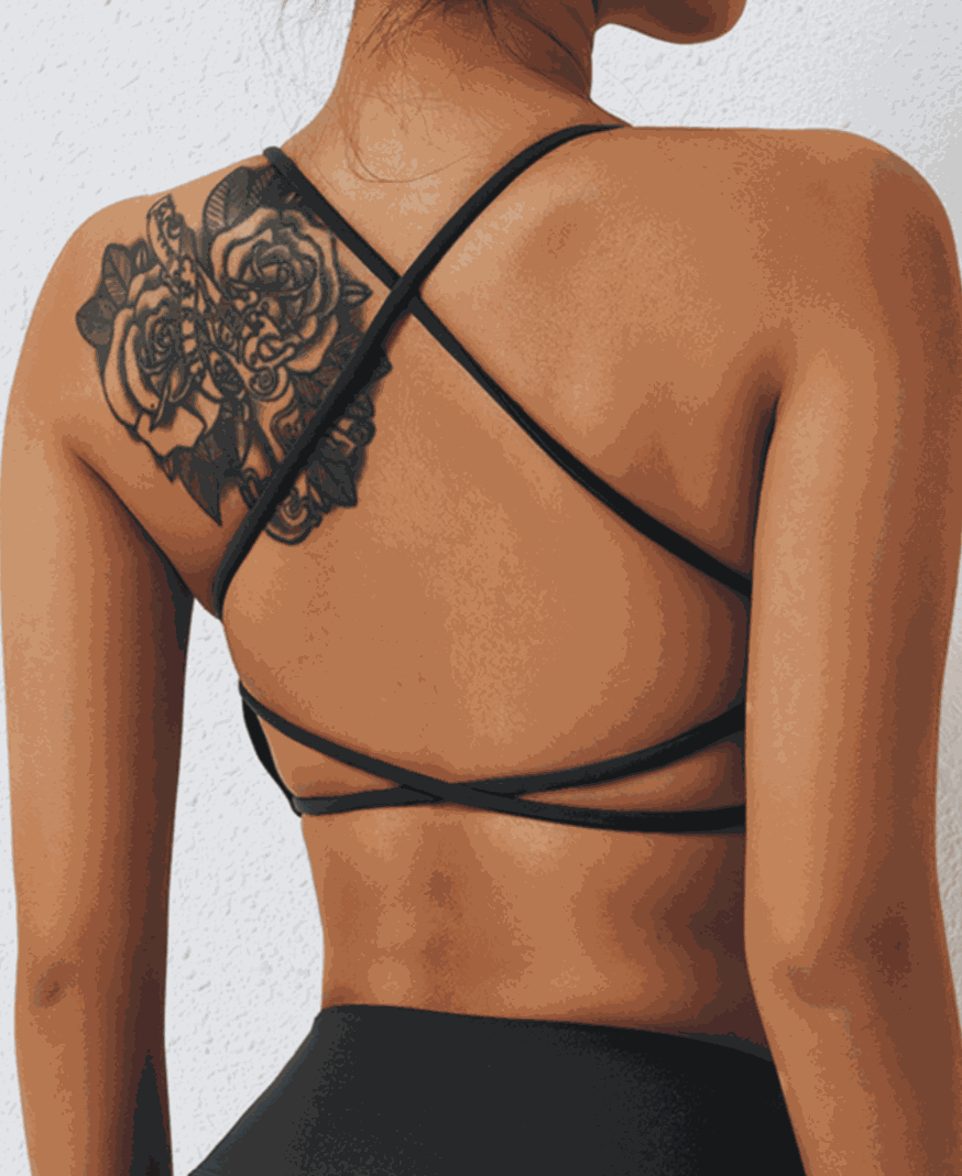 Woman wearing minimal strappy black X Back Sports Bra with tattoo on shoulder