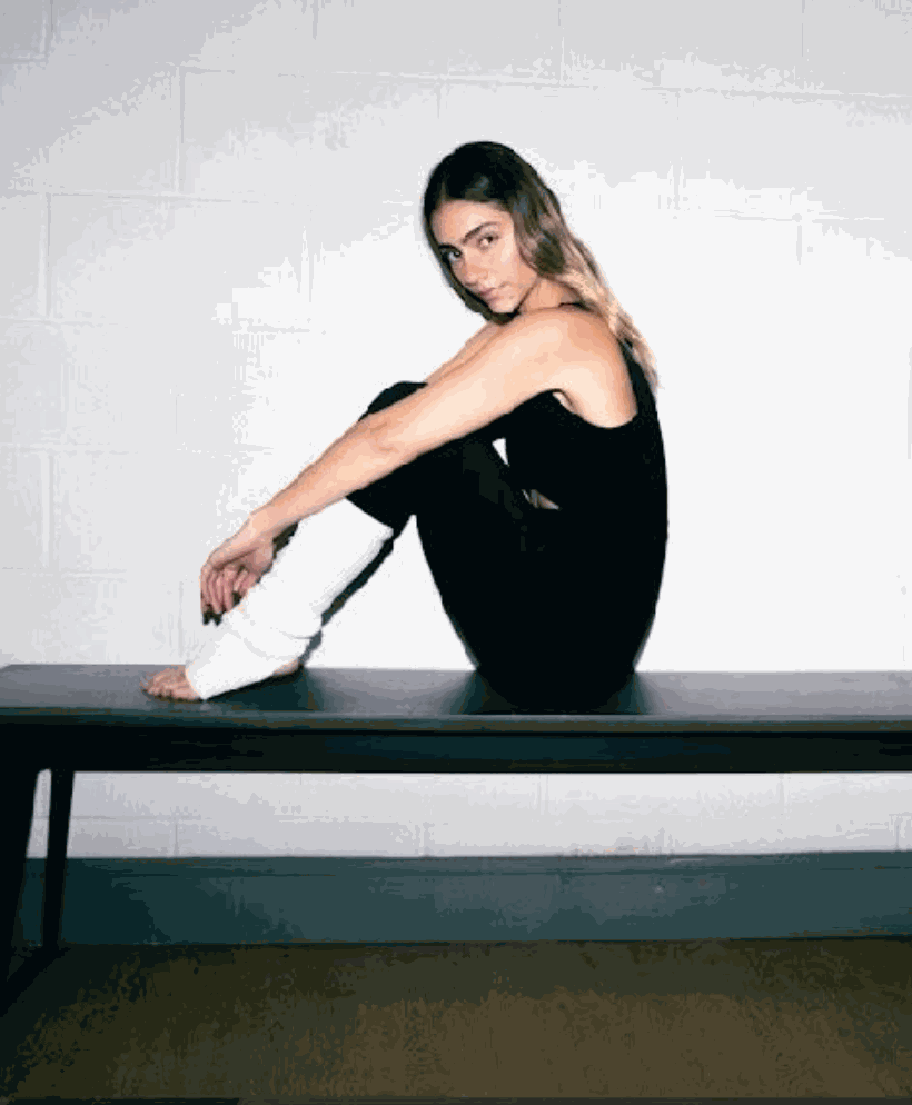 Woman wearing a black Deep V Reversible Body Suit sitting on a bench with white leg warmers