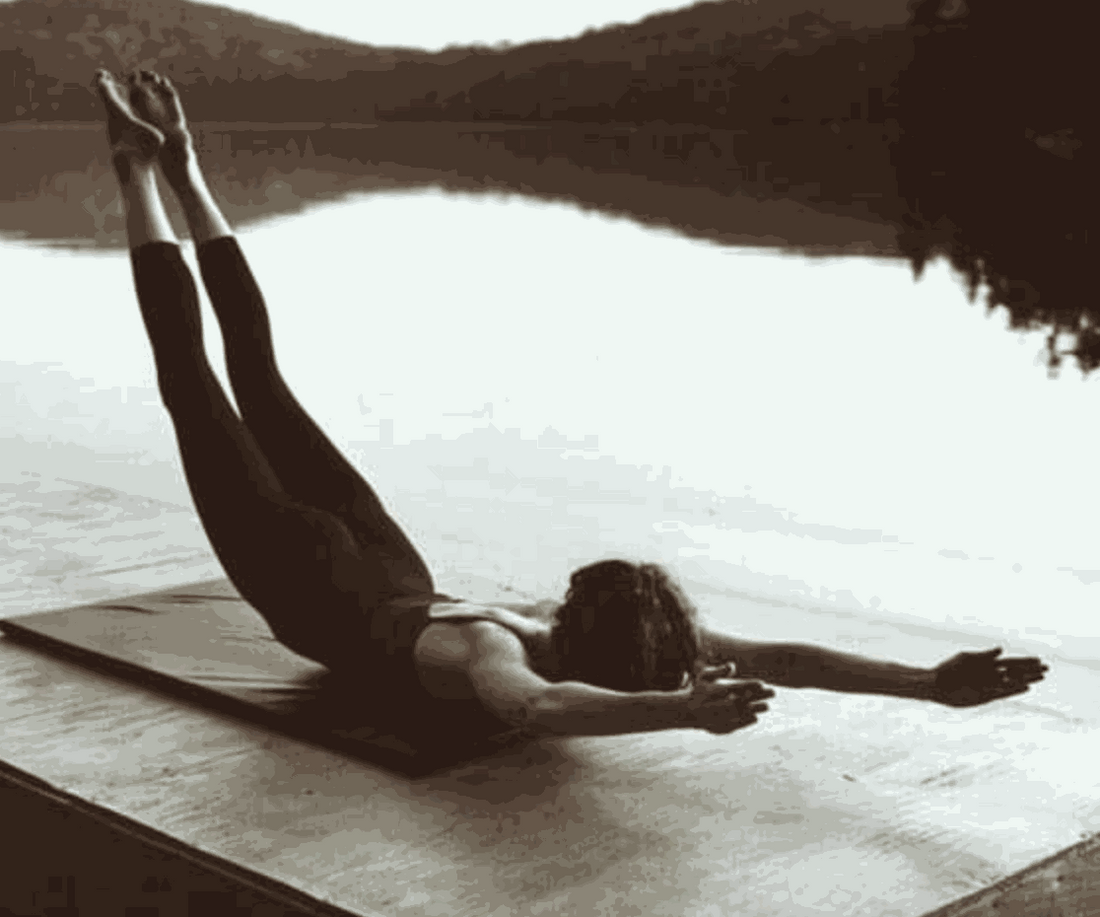 Person performing Pilates back extension exercise on mat by water at Upper-Hand Mat Workshop