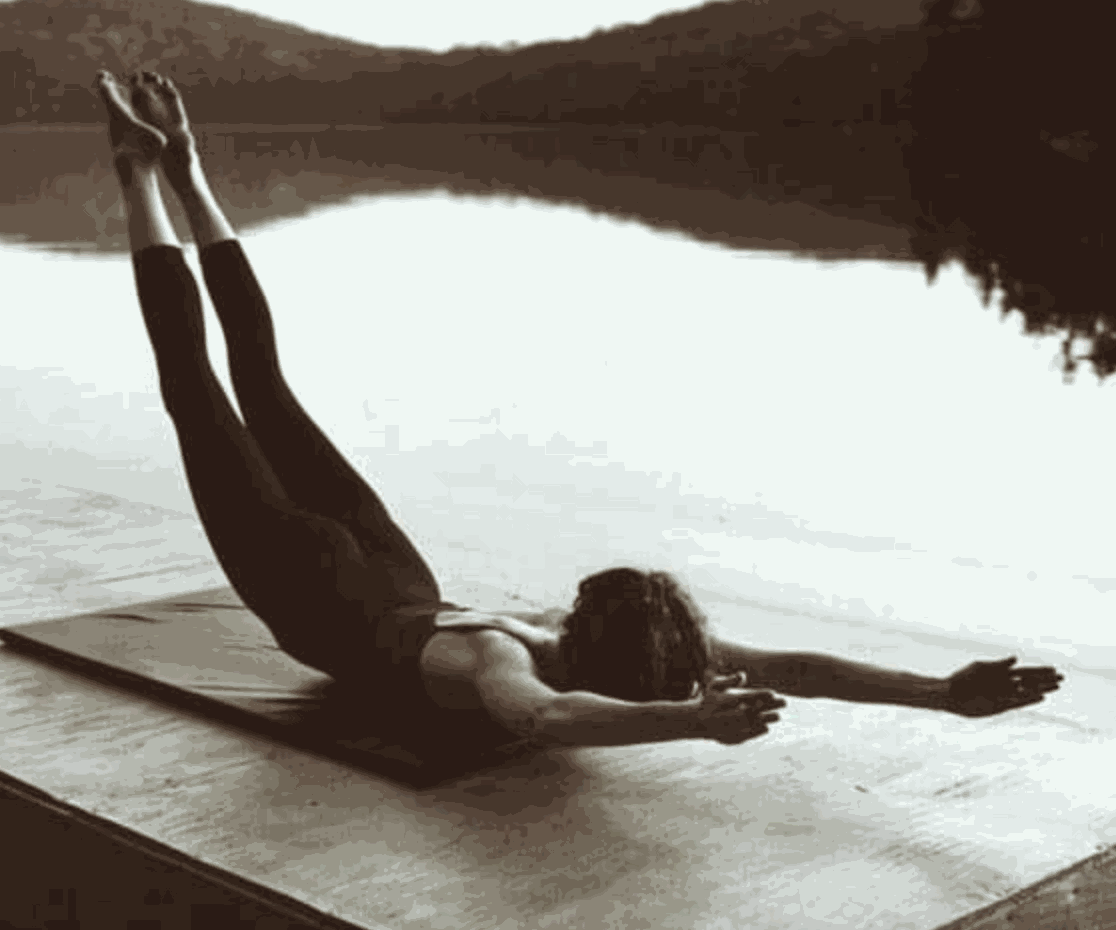 Person performing Pilates back extension exercise on mat by water at Upper-Hand Mat Workshop