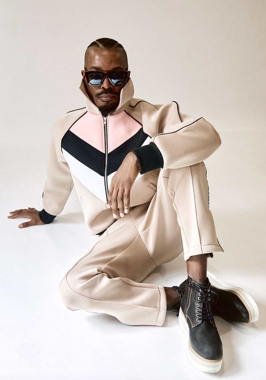 The Brooklyn Jacket beige sustainable techno fabric with SPF 50, front zipper, contrast piping, and two pockets, worn by model with matching pants and black boots